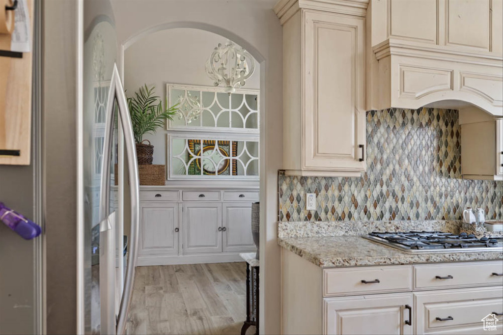 Kitchen featuring stainless steel appliances, light wood-style flooring, tasteful backsplash, light stone counters, and arched walkways
