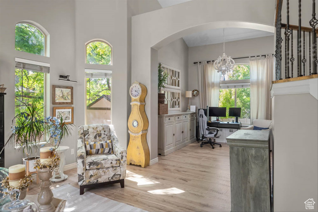 Office area featuring arched walkways, plenty of natural light, light wood-style flooring, a chandelier, and a towering ceiling