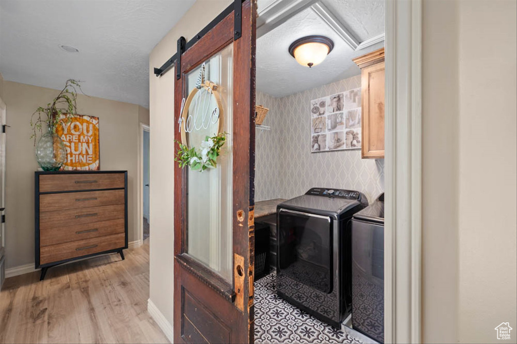 Laundry room with washing machine and dryer, a barn door, light wood finished floors, cabinet space, and wallpapered walls