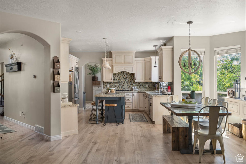 Kitchen featuring cream cabinets, tasteful backsplash, light wood finished floors, a center island, and a textured ceiling