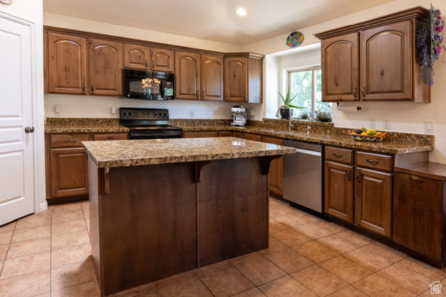 Kitchen with black appliances, a center island, light tile patterned flooring, recessed lighting, and a breakfast bar