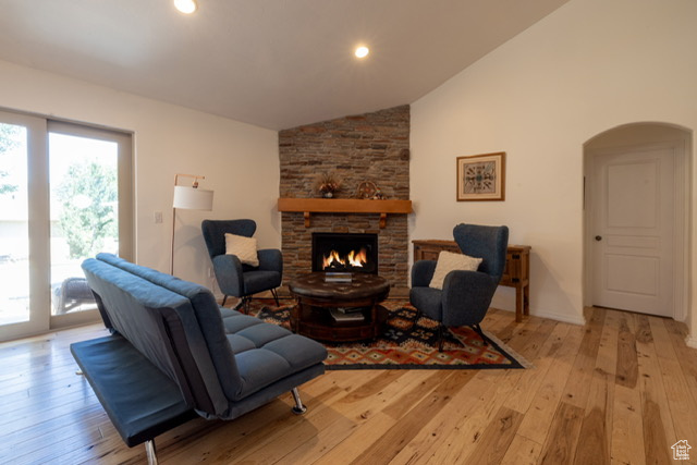 Living room featuring lofted ceiling, arched walkways, light wood-type flooring, a stone fireplace, and recessed lighting