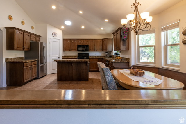 Kitchen featuring black microwave, freestanding refrigerator, a center island, a chandelier, and recessed lighting