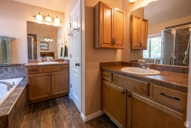 Bathroom featuring two vanities, a shower stall, a bath, and wood finished floors