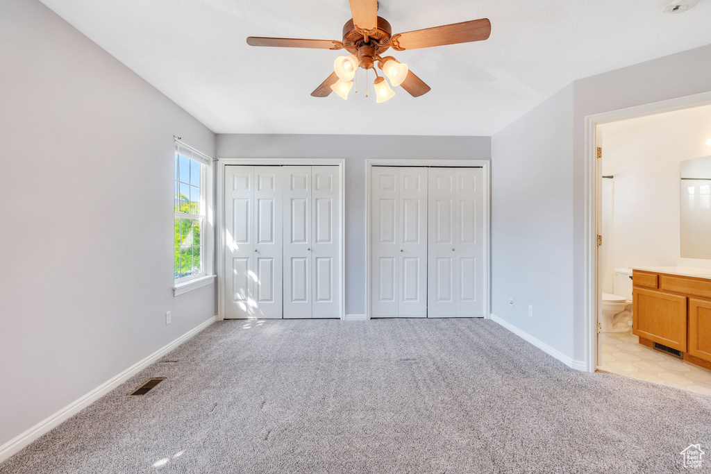 Unfurnished bedroom with light carpet, two closets, ensuite bath, and a ceiling fan