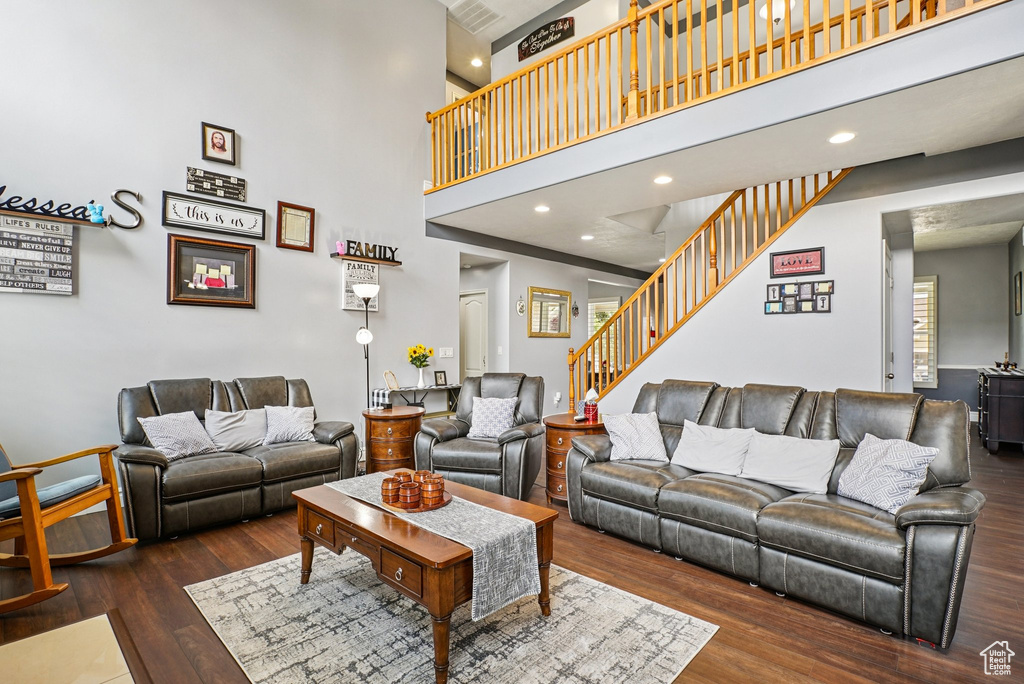 Living room with stairs, wood finished floors, a towering ceiling, and recessed lighting