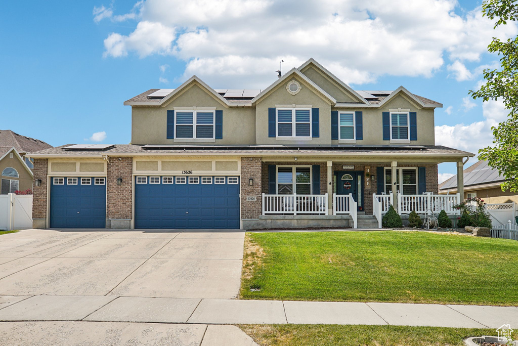 View of front of home with covered porch, roof mounted solar panels, concrete driveway, stucco siding, and brick siding