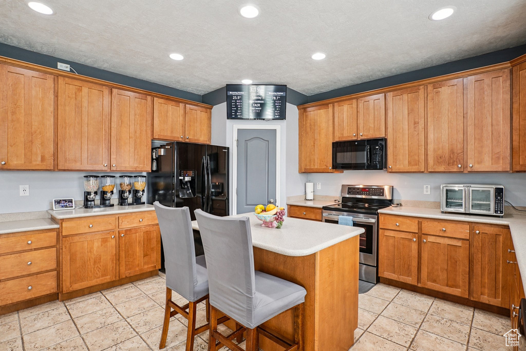 Kitchen featuring black appliances, a kitchen bar, light countertops, brown cabinetry, and recessed lighting