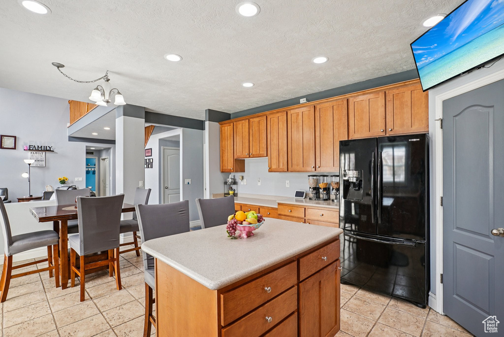 Kitchen with black refrigerator with ice dispenser, a kitchen island, light countertops, recessed lighting, and brown cabinetry