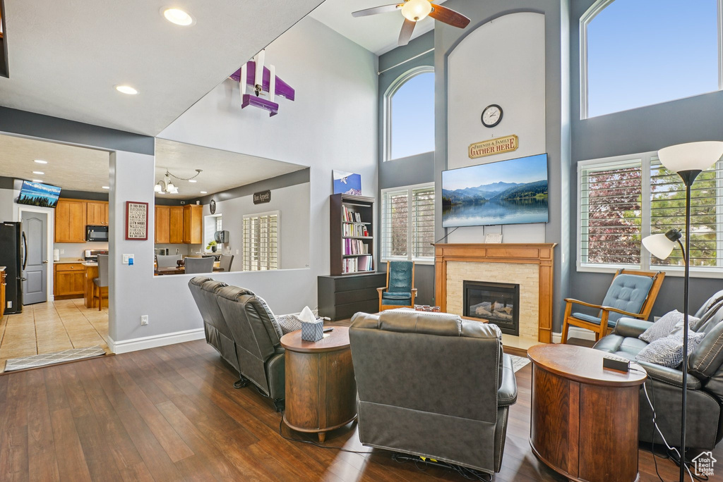 Living room with hardwood / wood-style floors, a glass covered fireplace, a high ceiling, plenty of natural light, and a ceiling fan