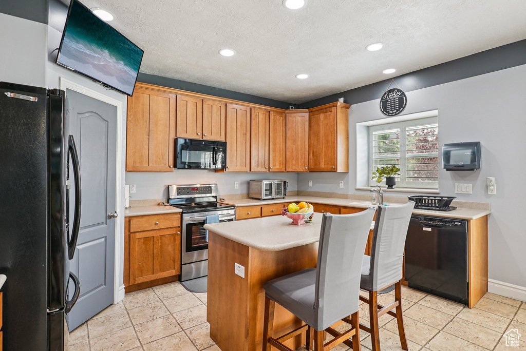 Kitchen with black appliances, light countertops, recessed lighting, a kitchen breakfast bar, and a kitchen island