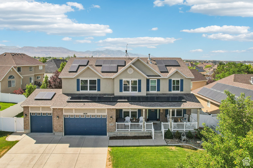 View of front of home with covered porch, roof mounted solar panels, concrete driveway, roof with shingles, and brick siding