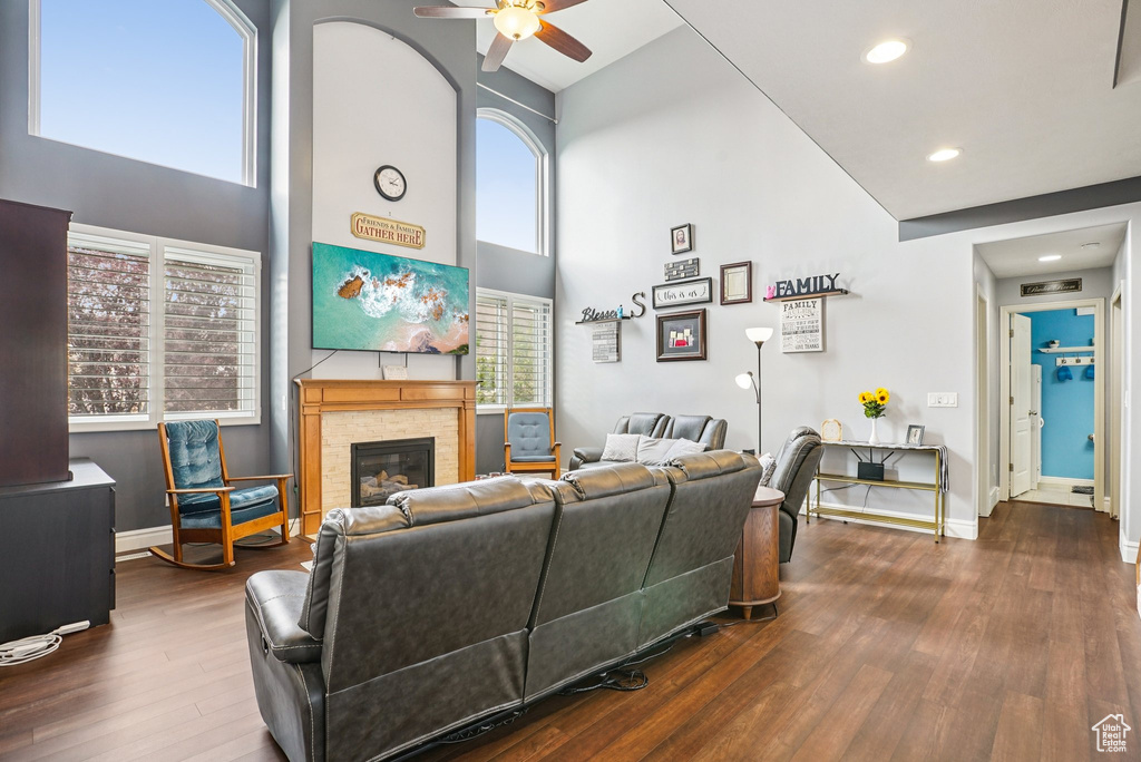 Living room with a high ceiling, ceiling fan, wood finished floors, a glass covered fireplace, and recessed lighting