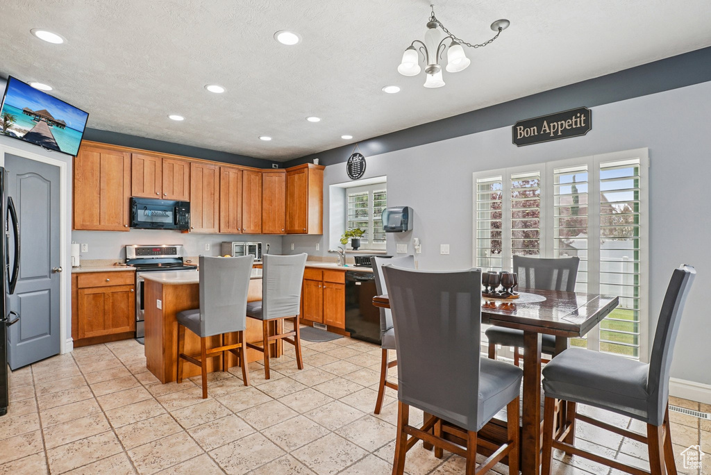 Kitchen with black appliances, a chandelier, recessed lighting, a kitchen island, and brown cabinets