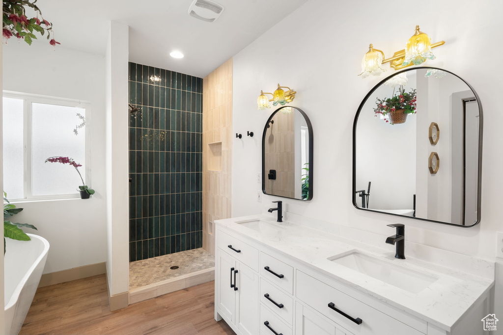 Bathroom featuring double vanity, a freestanding tub, tiled shower, wood finished floors, and recessed lighting
