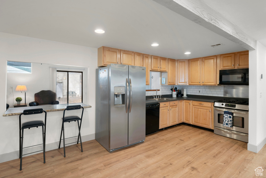 Kitchen with black appliances, light wood-style floors, light brown cabinetry, decorative backsplash, and recessed lighting