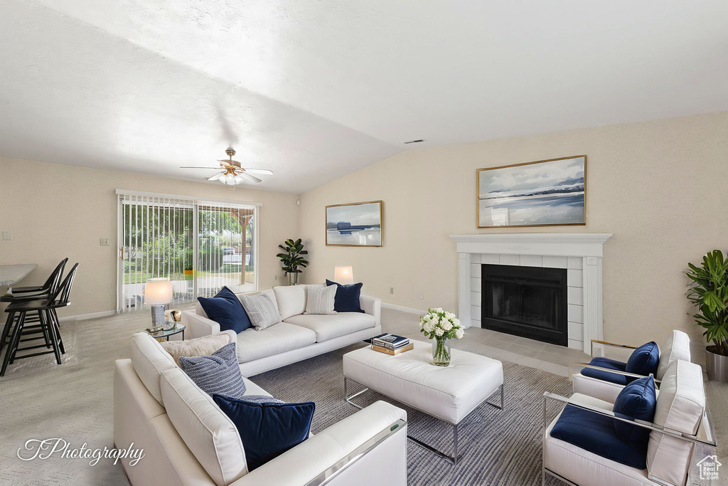 Living room with vaulted ceiling, a ceiling fan, a tile fireplace, and light carpet