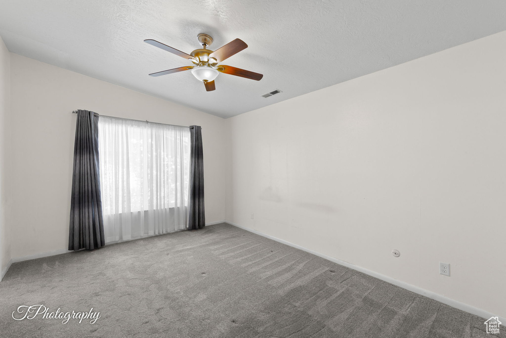 Empty room with carpet floors, a ceiling fan, vaulted ceiling, and a textured ceiling