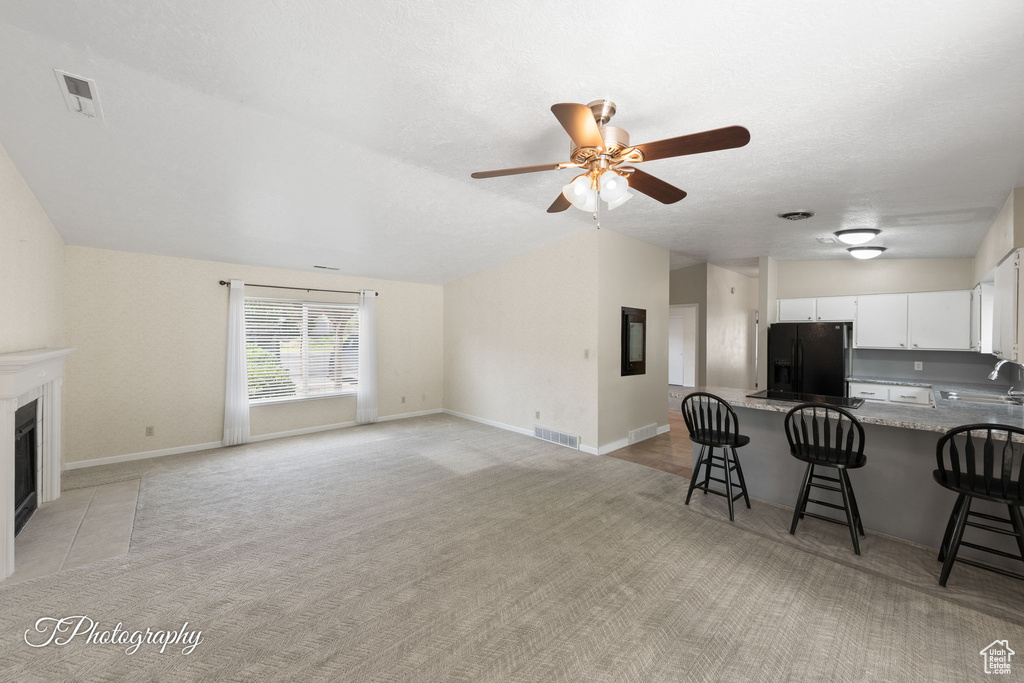 Living room with light colored carpet, ceiling fan, and a tiled fireplace