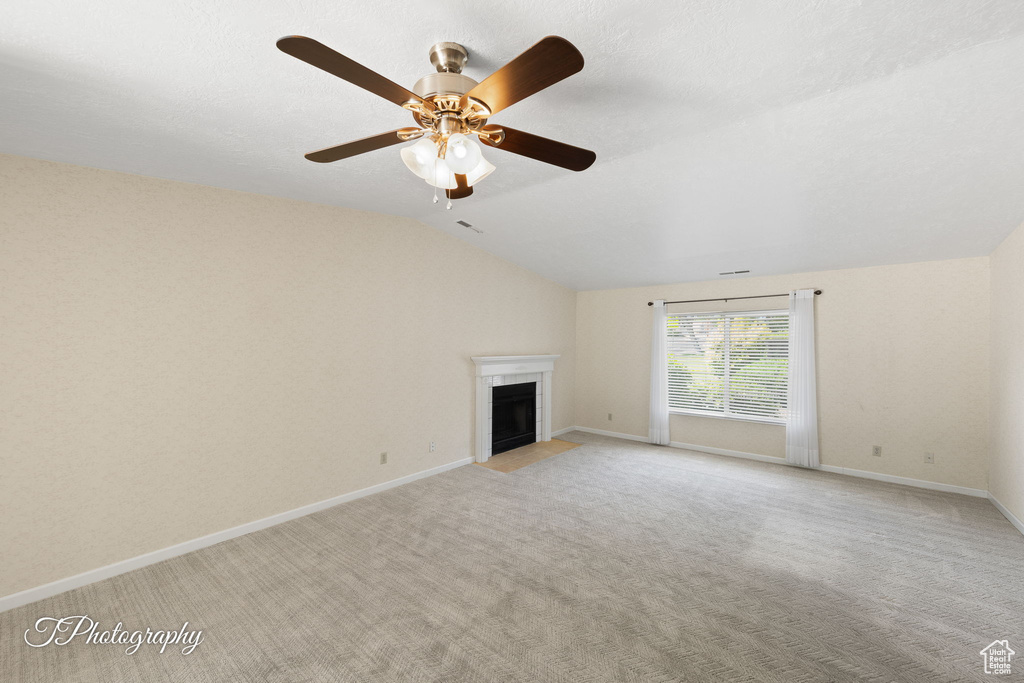 Unfurnished living room featuring vaulted ceiling, a fireplace, light colored carpet, and a ceiling fan