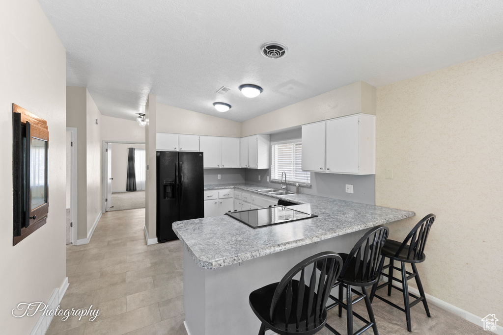 Kitchen with black appliances, a peninsula, light countertops, white cabinets, and a breakfast bar