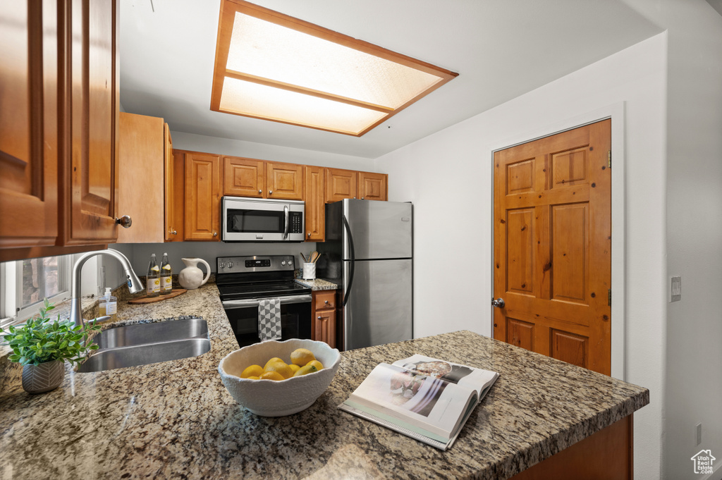 Kitchen featuring appliances with stainless steel finishes, brown cabinets, a peninsula, and light stone counters