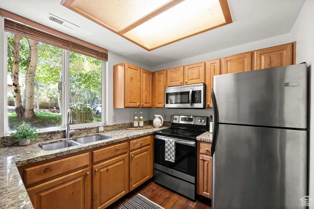 Kitchen featuring appliances with stainless steel finishes, light stone countertops, dark wood finished floors, and brown cabinets