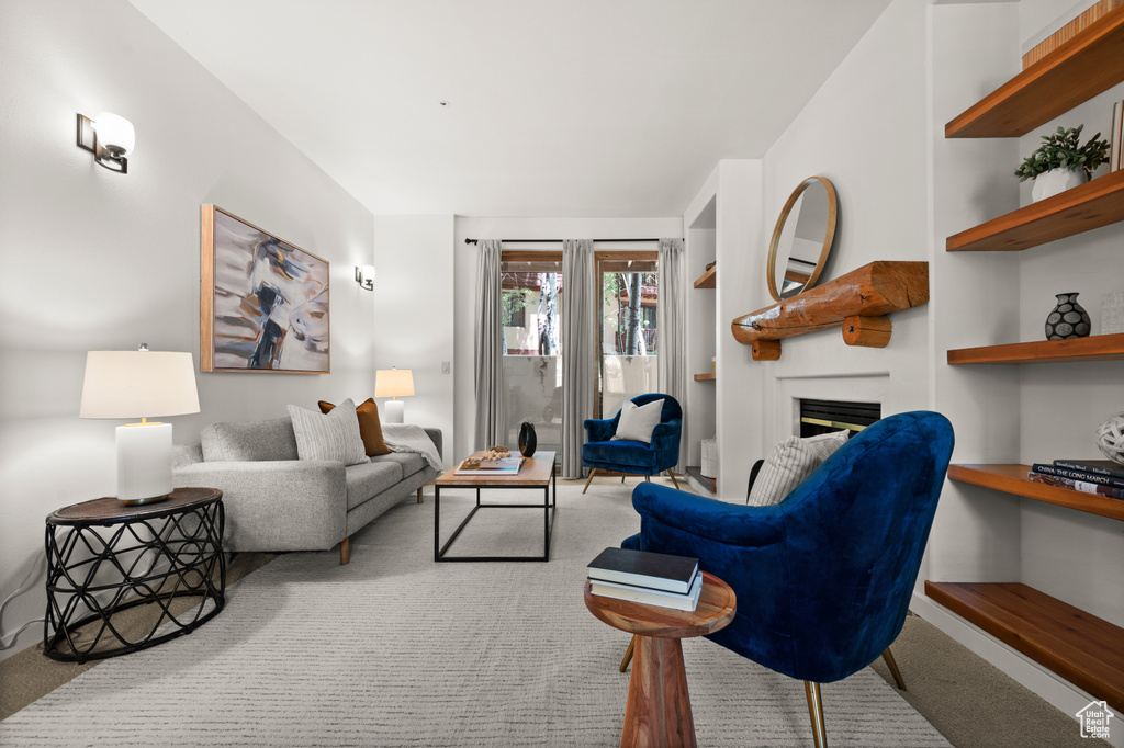 Carpeted living area featuring a glass covered fireplace and baseboards