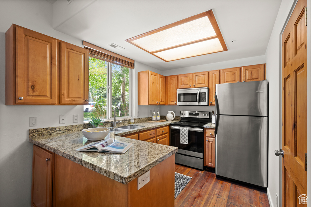 Kitchen with stainless steel appliances, a peninsula, dark wood-style flooring, and brown cabinets