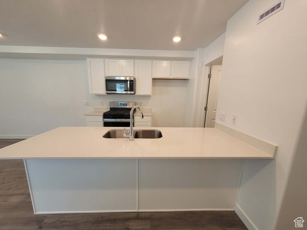 Kitchen with stainless steel appliances, white cabinetry, a peninsula, dark wood-style floors, and recessed lighting