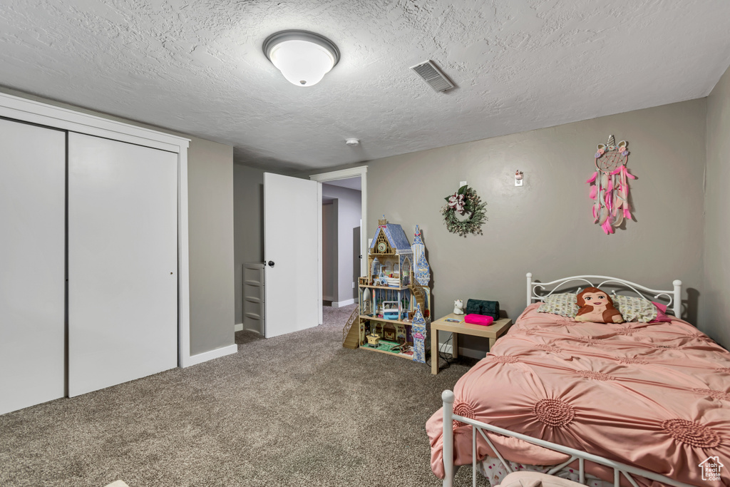 Carpeted bedroom featuring a textured ceiling and a closet