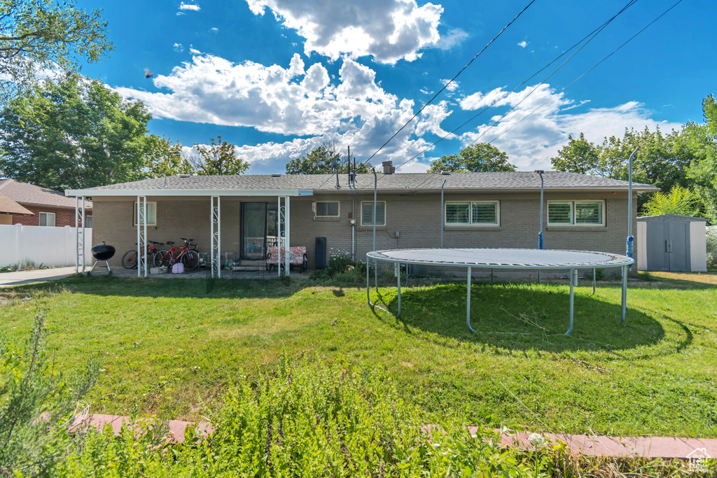 Back of property featuring a shed, a trampoline, a patio, and brick siding