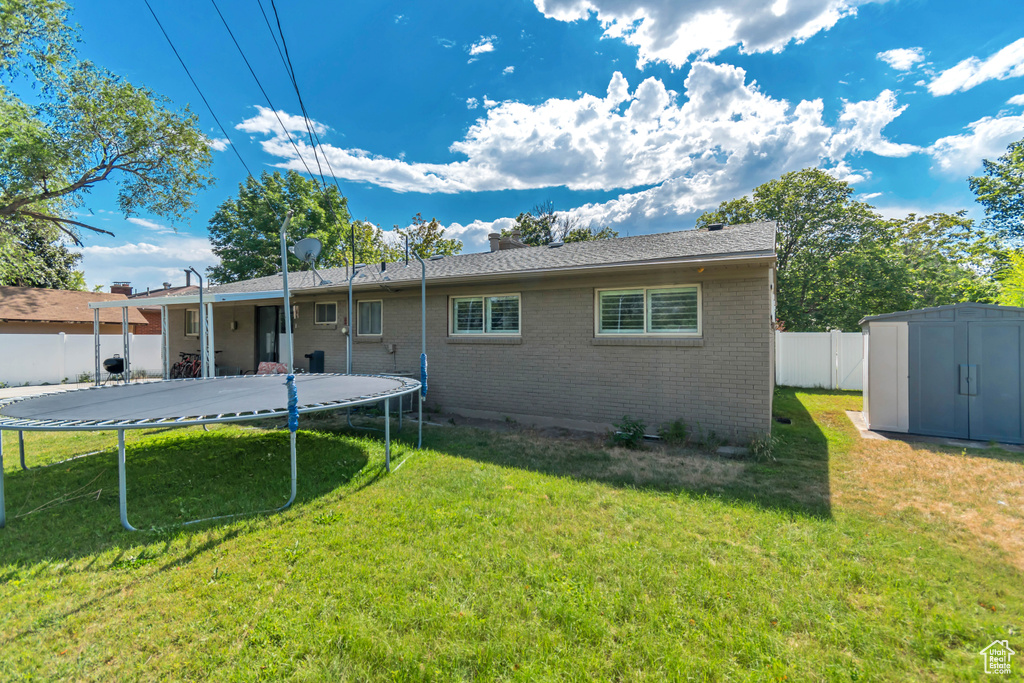 Back of property featuring a trampoline, brick siding, and a storage shed