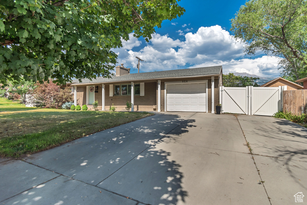 Single story home with concrete driveway, an attached garage, a gate, a chimney, and brick siding
