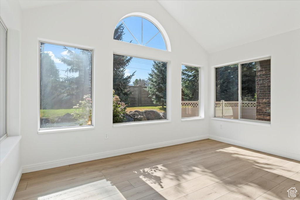 Unfurnished sunroom with wood finished floors and high vaulted ceiling