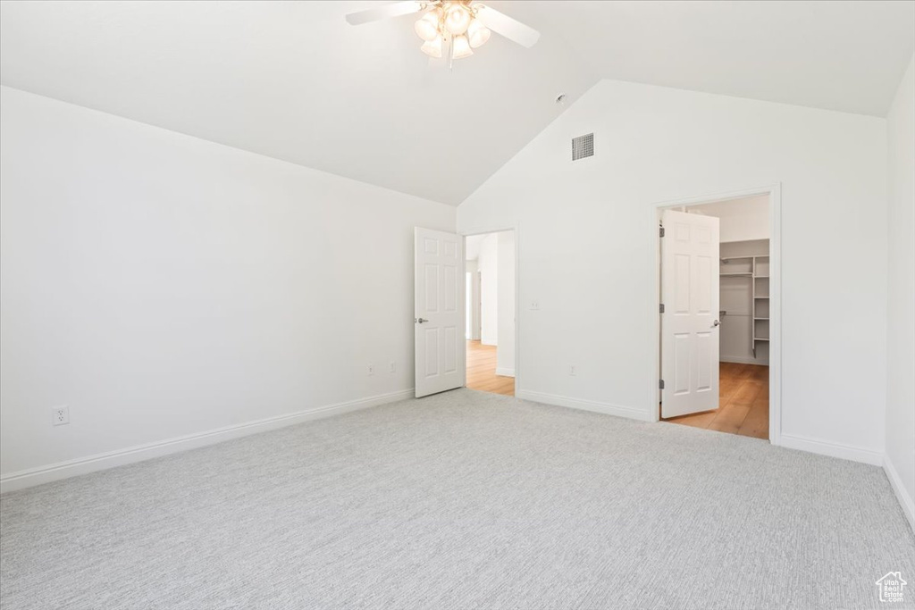 Unfurnished bedroom with a walk in closet, high vaulted ceiling, light colored carpet, ceiling fan, and a closet
