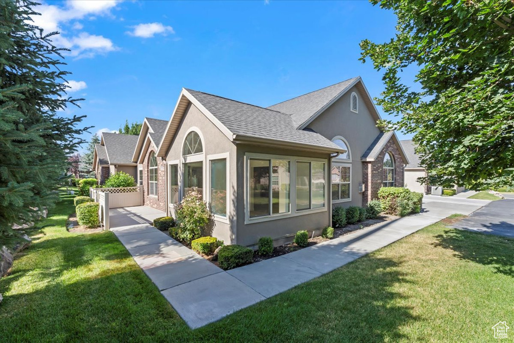 View of property exterior with stucco siding, a yard, and roof with shingles