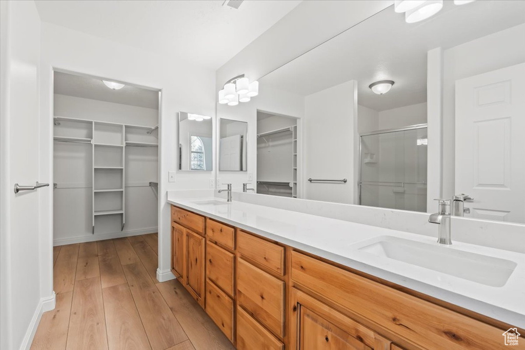 Bathroom with a walk in closet, double vanity, a stall shower, and wood-type flooring