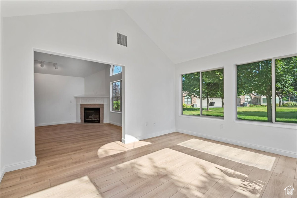 Unfurnished living room with wood finished floors, high vaulted ceiling, and a tiled fireplace
