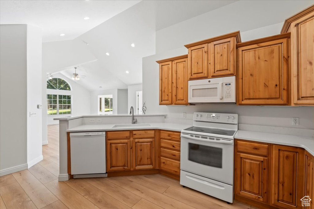 Kitchen with white appliances, light wood finished floors, a peninsula, brown cabinets, and vaulted ceiling
