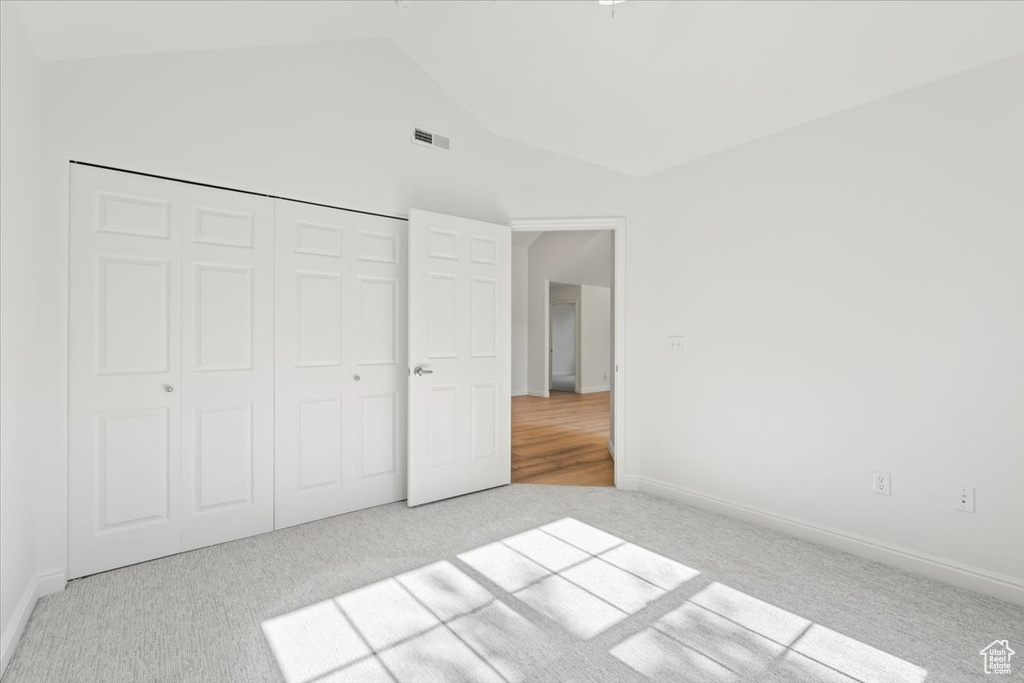 Unfurnished bedroom featuring carpet floors, vaulted ceiling, and a closet