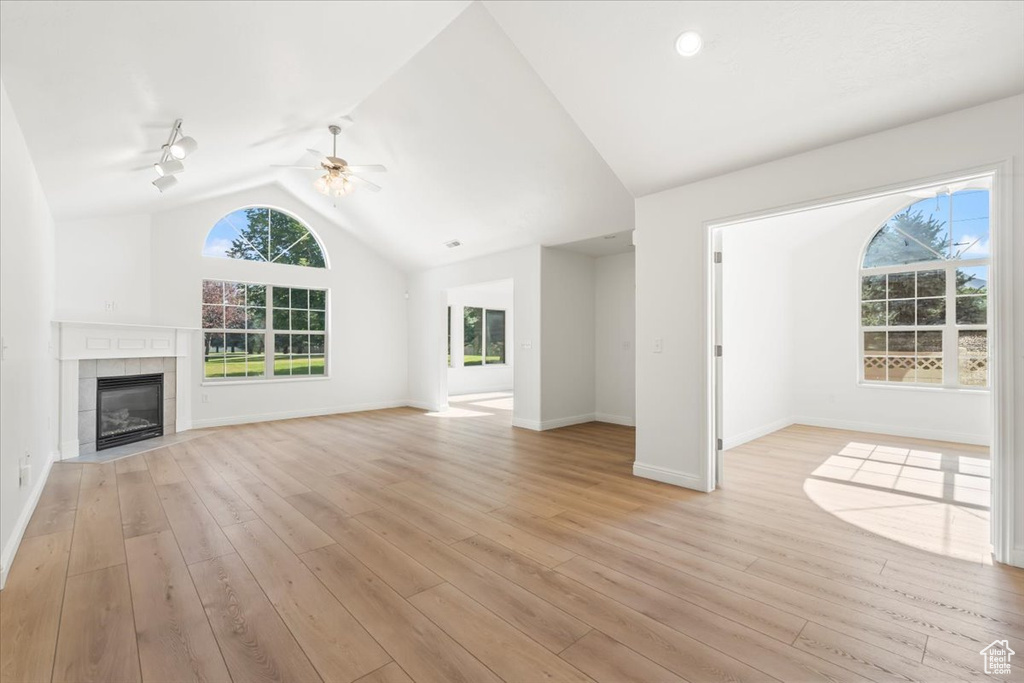 Unfurnished living room featuring vaulted ceiling, ceiling fan, light wood-style floors, a fireplace, and track lighting