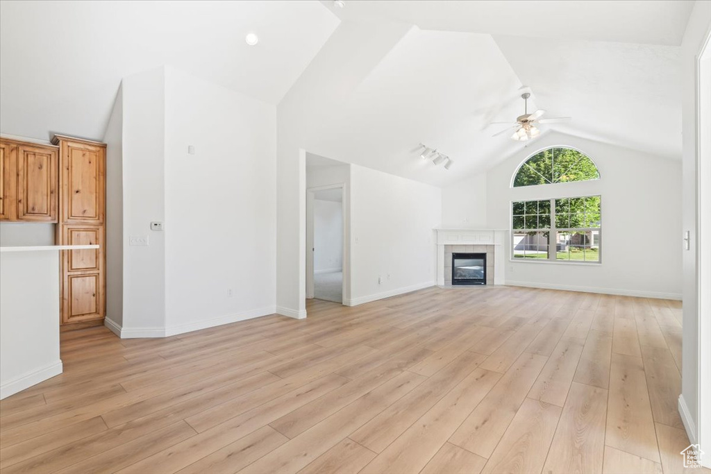 Unfurnished living room featuring vaulted ceiling, a ceiling fan, light wood-style floors, and a fireplace