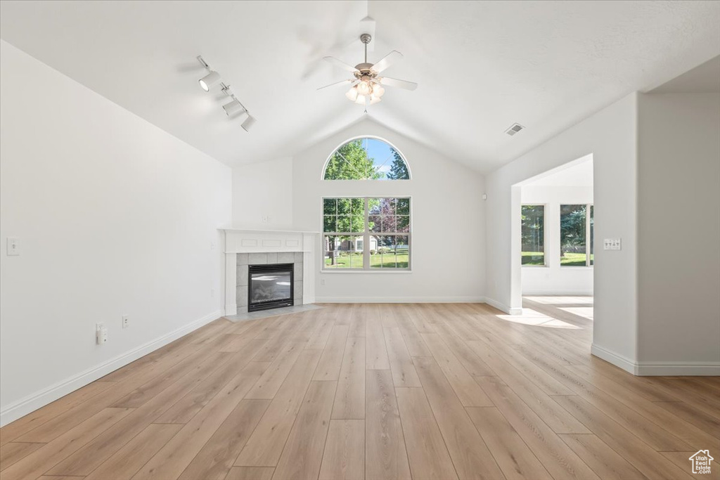Unfurnished living room featuring ceiling fan, vaulted ceiling, a fireplace, light wood-style flooring, and rail lighting