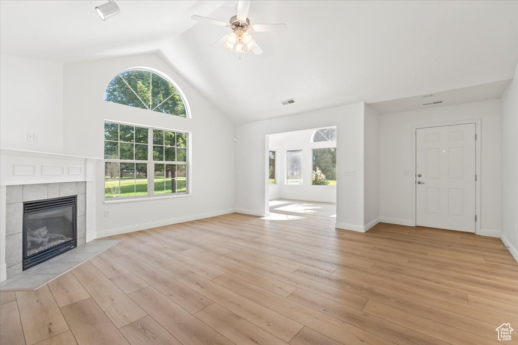 Unfurnished living room featuring a ceiling fan, a tile fireplace, light wood-style flooring, and high vaulted ceiling