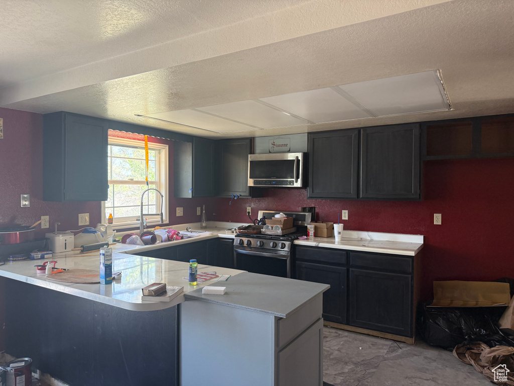 Kitchen with appliances with stainless steel finishes, a peninsula, light countertops, and a textured ceiling