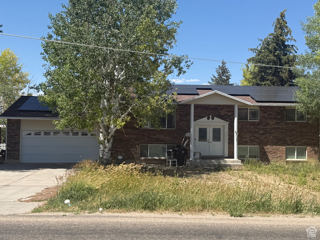 Bi-level home with roof mounted solar panels, concrete driveway, brick siding, and a garage