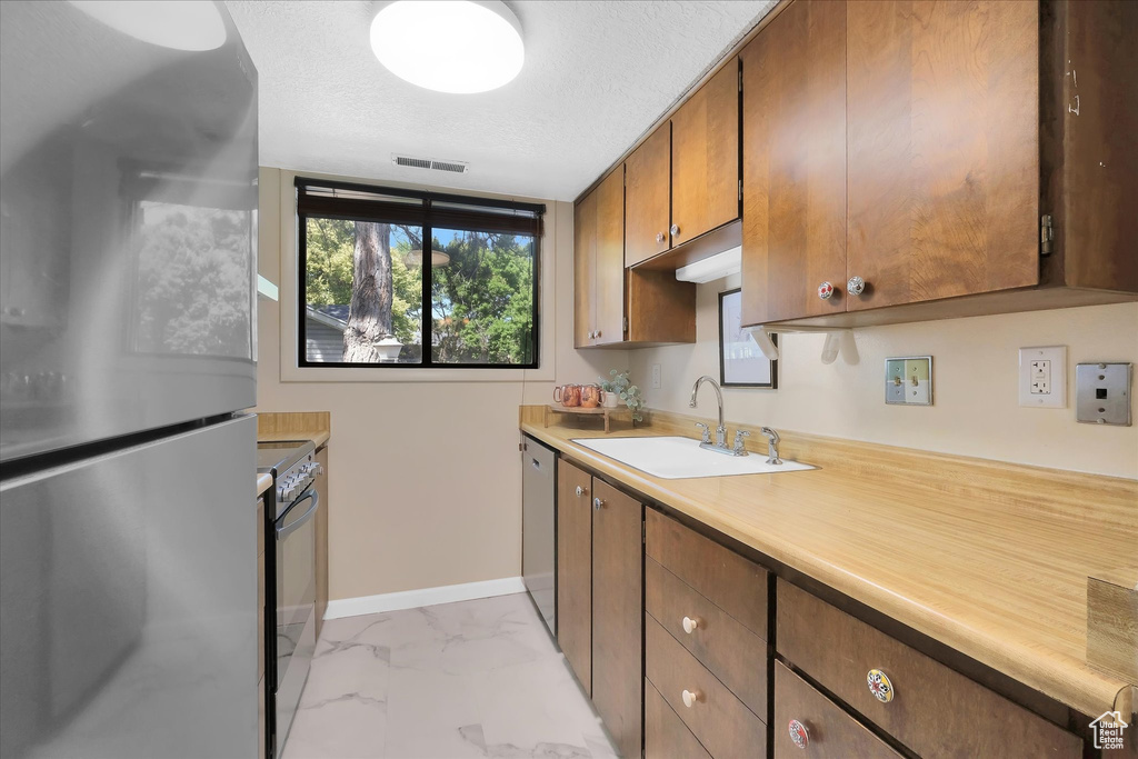 Kitchen with appliances with stainless steel finishes, light marble finish flooring, light countertops, and brown cabinetry