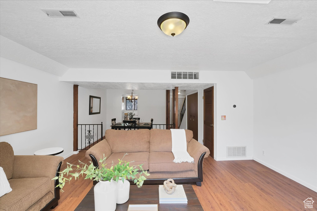 Living room featuring a chandelier, wood finished floors, a textured ceiling, and lofted ceiling