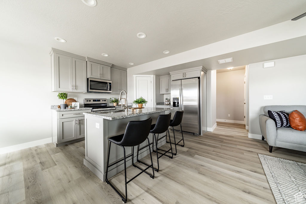 Kitchen with stainless steel appliances, gray cabinetry, light stone counters, a breakfast bar, and recessed lighting